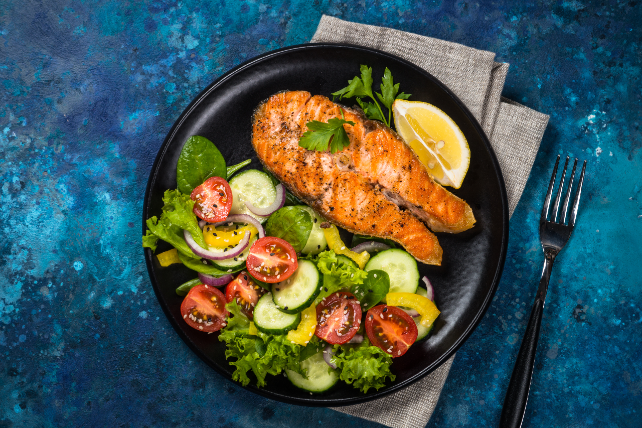 Trancio di salmone grigliato servito con insalata su sfondo blu.