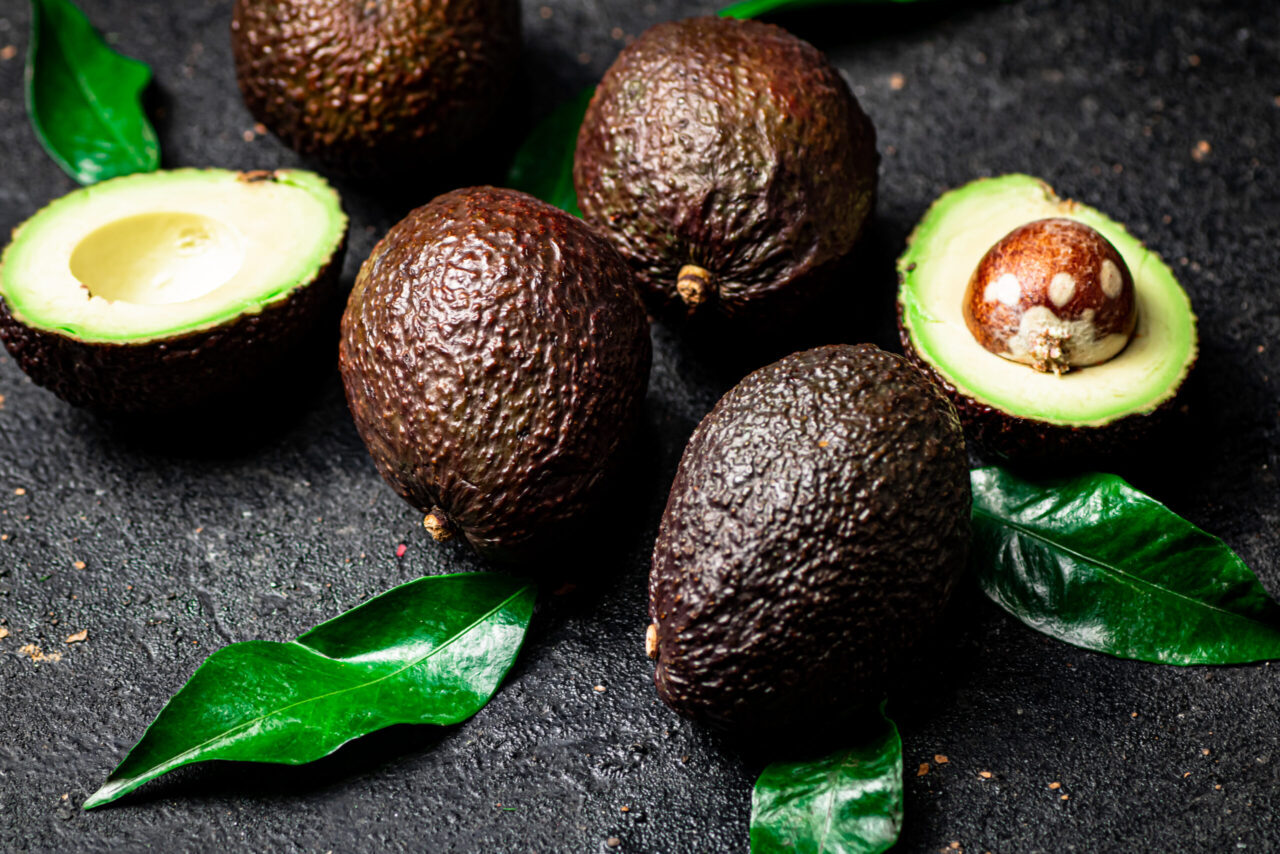 Avocado maturi con foglie su sfondo nero