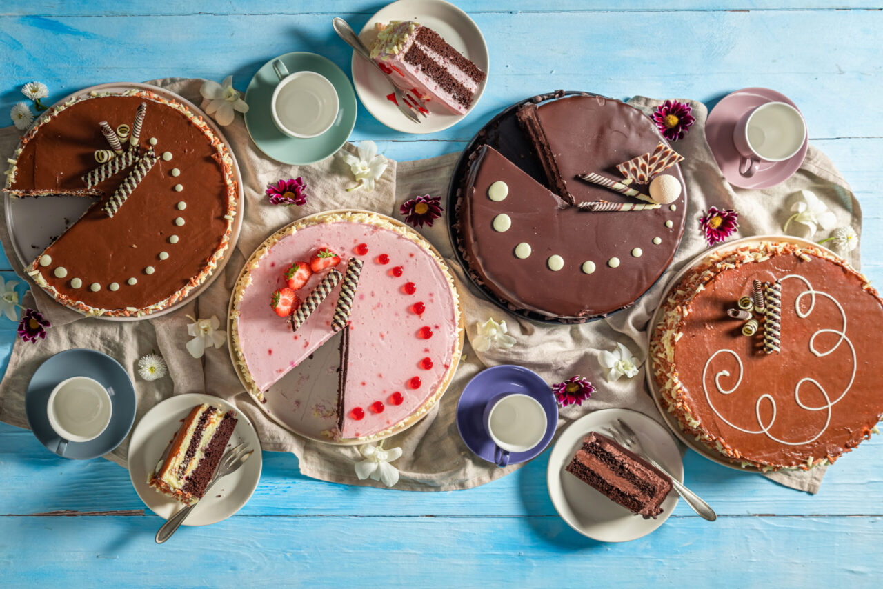 Torte industriali alla fragola, al cioccolato e al caramello servite con caffè su una tavola di legno azzurro